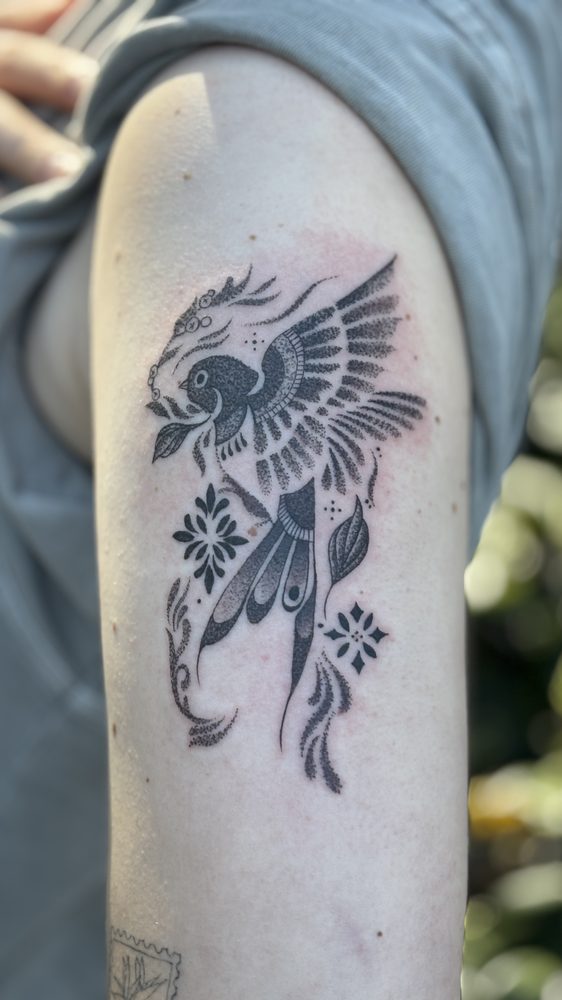 Black-and-grey dotwork bird in flight with decorative flowers